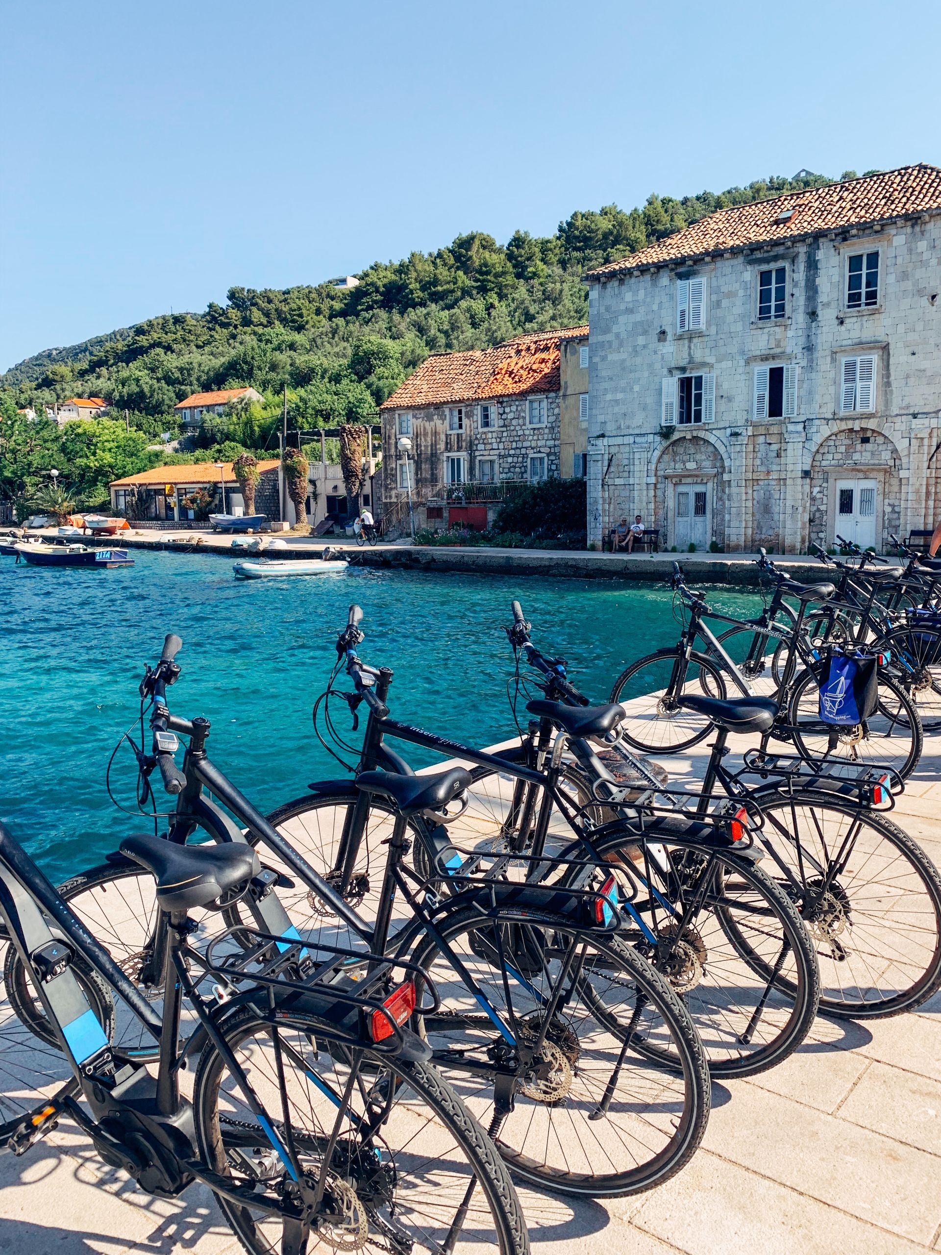 Fahrräder, die entlang einer Küstenstraße in einem Küstendorf geparkt sind, Fahrrad und Boot in Kroatien, Dalmatien